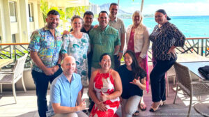 Smiling group gathered on a tropical balcony with ocean and beach in the background.